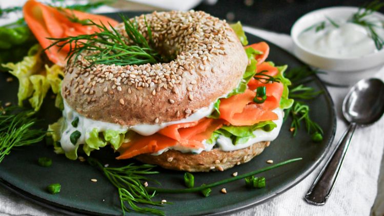 Bagel gefüllt mit Karottenlachs, Salat und Creme auf Teller